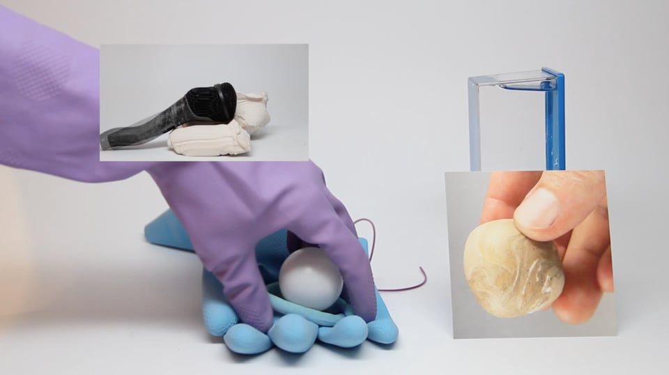 A video still of several different images collaged on top of one another. In the background, a gloved hand places a white ball inside another glove. In another image, a hand holds a stone or shell. In another, what looks like a melted microphone lays atop a miniature white bag.