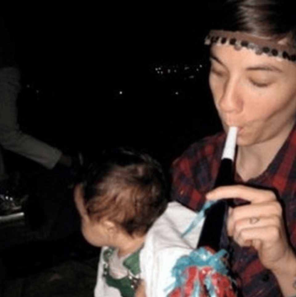 a blurry snapshot of a person in a plaid shirt holding a baby while blowing a party horn
