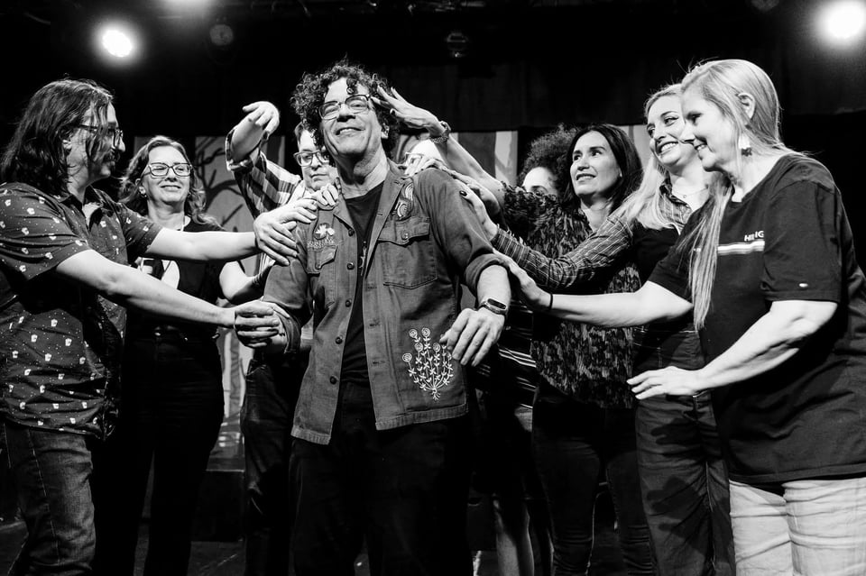 black and white photo of roy on stage, getting gently touched by the cast of Austin Secrets