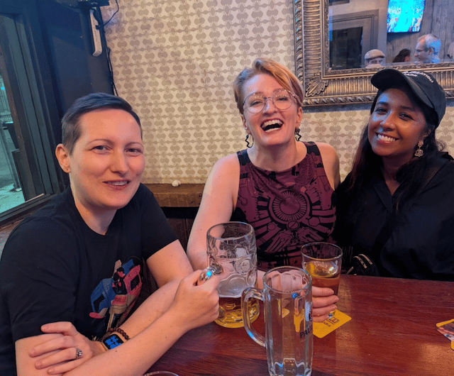 Jess, Maya Murphy, and Mitu Khandaker smiling and laughing with drinks around a table at a bar