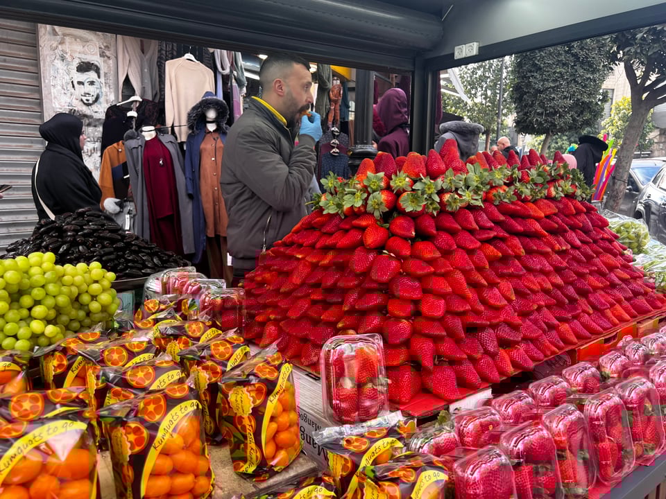 A fruit stand with a giant pile of huge strawberries, and some other fruit (oranges and grapes)