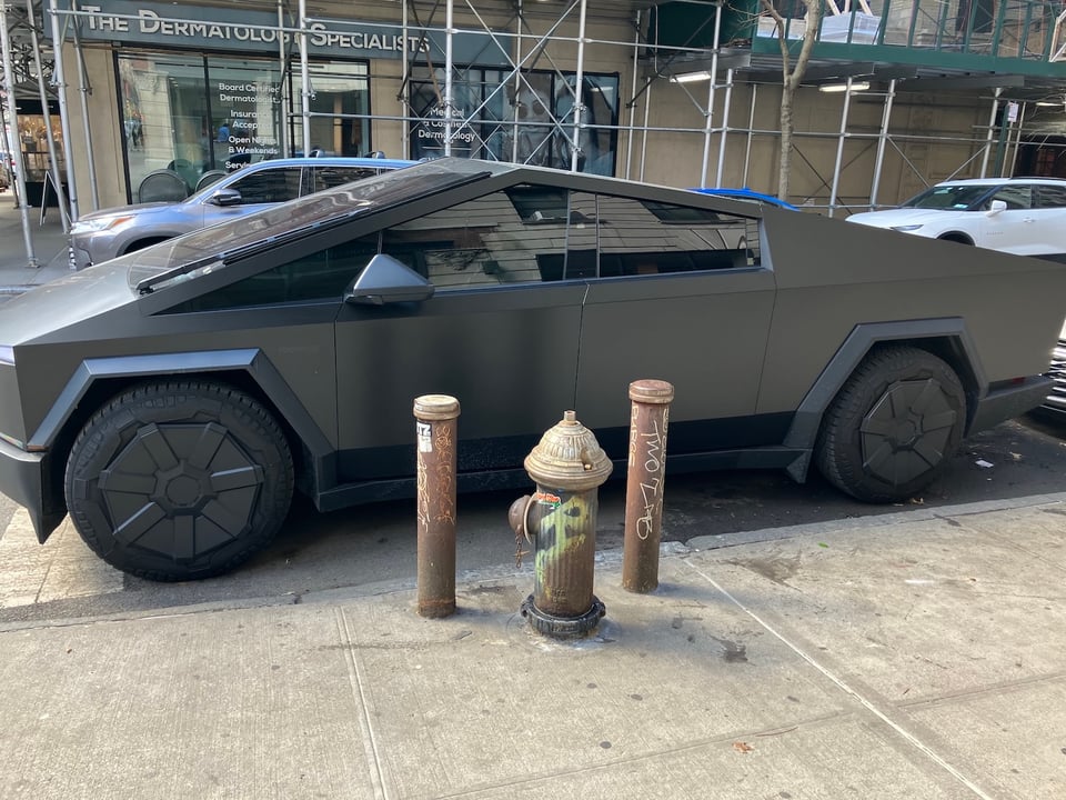 A matte-gray Cybertruck parked in front of a fire hydrant on a Manhattan street.