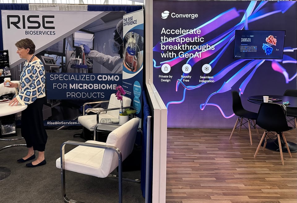 Two booths at a trade show, with a low partition between; the one on the left is RISE Bioservices and the one on the right is CONVERGE