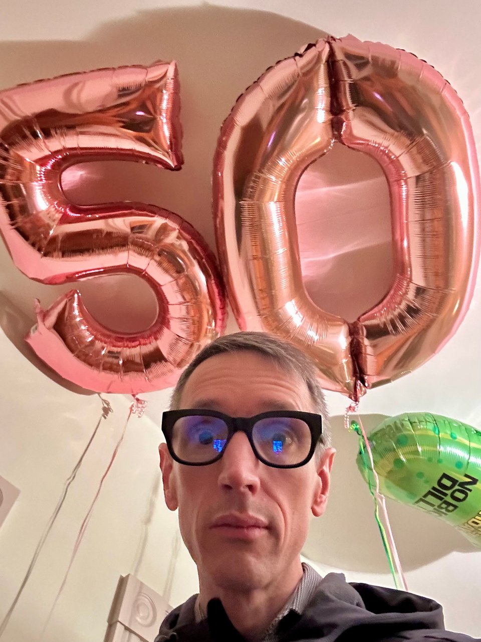 Selfie with two large balloons, one in the shape of a 5, one in the shape of a 0 floating above me