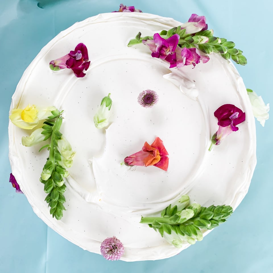 A vanilla-frosted round layer cake arrayed with edible flowers