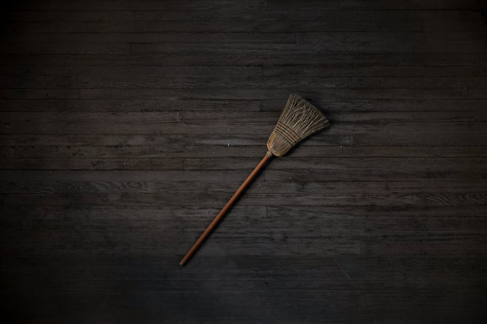 A broom lays on a grey wooden floor.