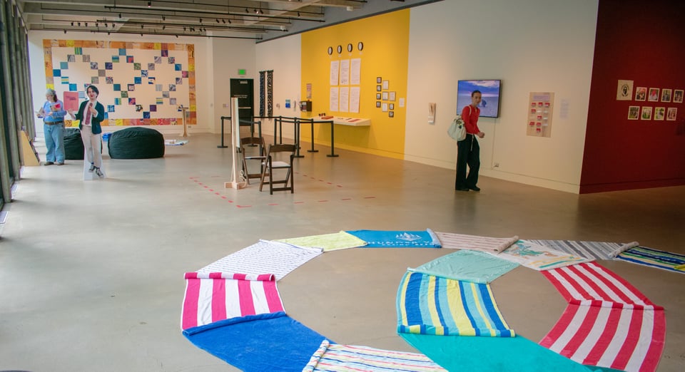 an installation view of the museum with towel sculptures, a cut out of simeen, chairs, stanchions, and banners