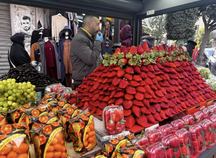 A fruit stand with a giant pile of huge strawberries, and some other fruit (oranges and grapes)