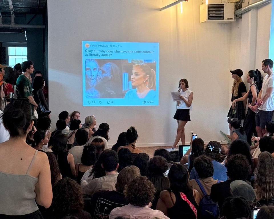 Mackenzie reading in front of a projection of a Tweet, a rapt, hot crowd looking on.