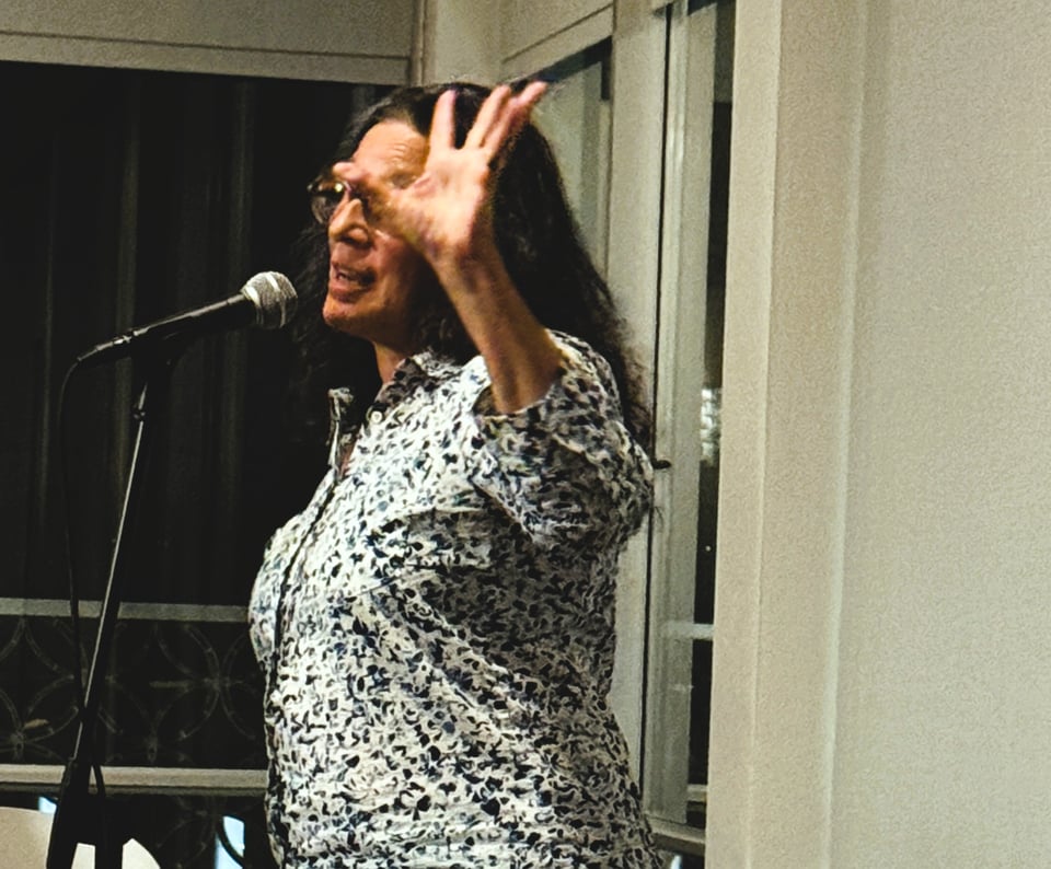 Me, at the mic, one hand in the air while I tell a story.