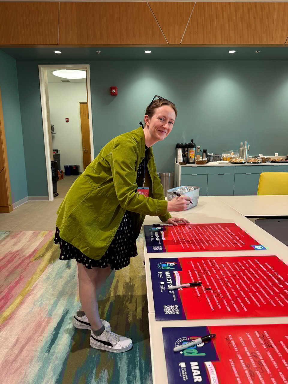 Me, wearing a moon phases dress, a chartreuse overshirt, and white sneakers, posing after signing festival posters.