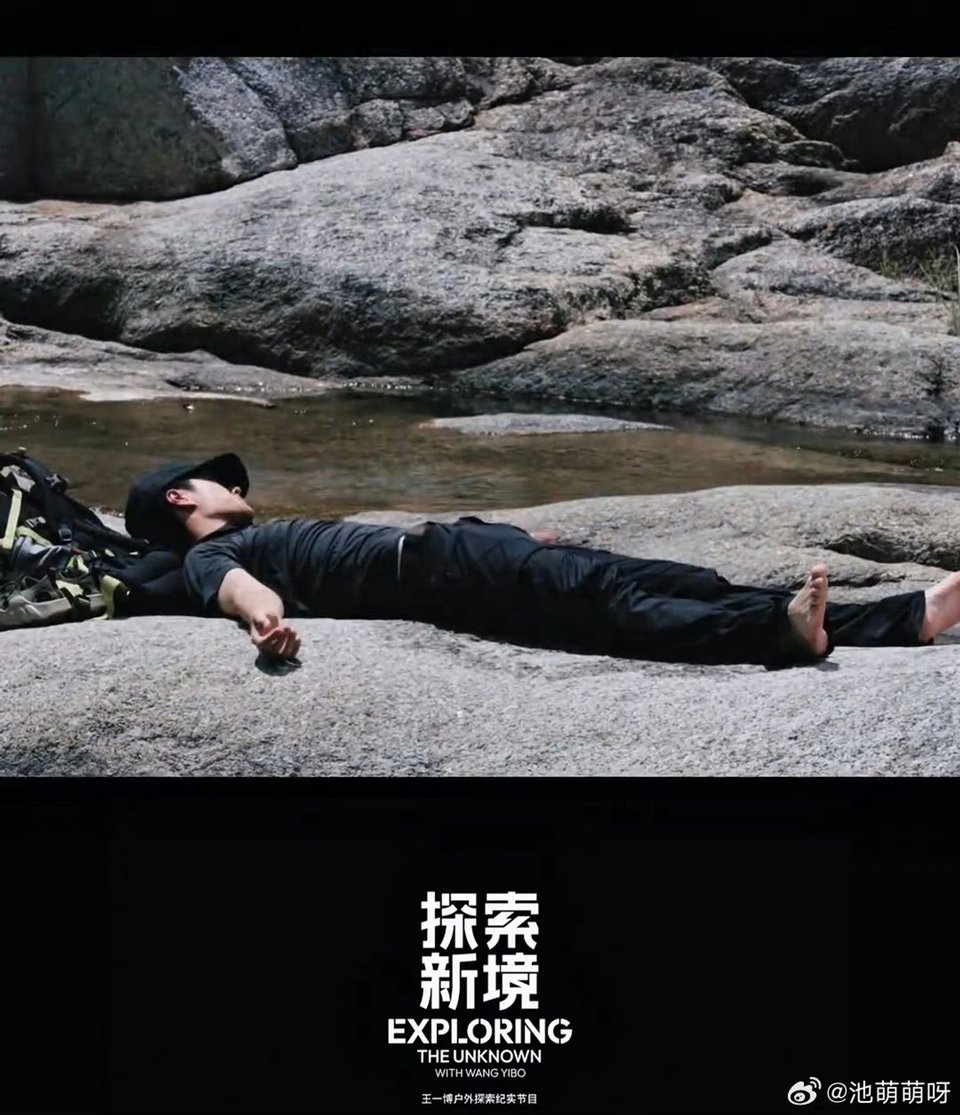 Photo of Yibo, dressed in black with a black cap, lying totally flat on a large flat rock in the middle of a stream, with other large rocks in the background. The logo for Exploring the Unknown is beneath the image.