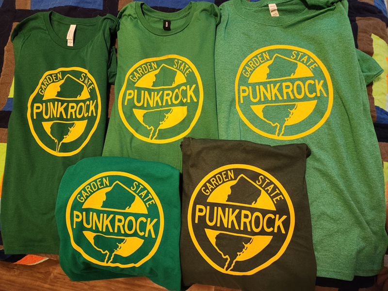 A photo of five different green t-shirts with the same Garden State Punk Rock logo printed on them in yellow.