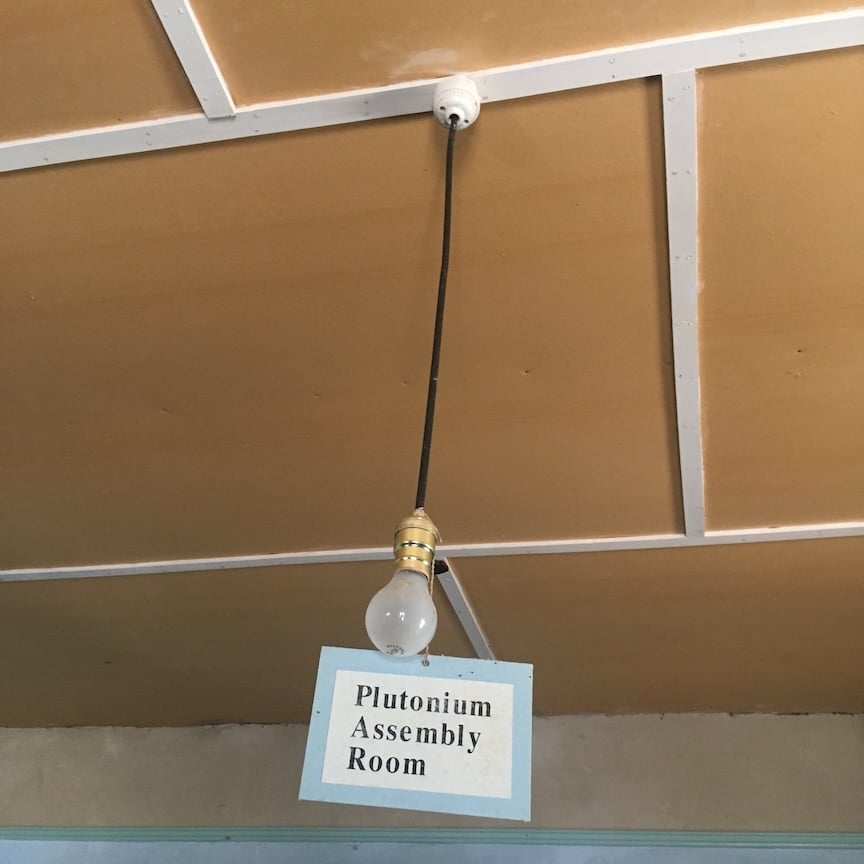 bare light blub hanging from ceiling in Gadget assembly room. A sign on the bulb proclaims Plutonium Assembly Room.