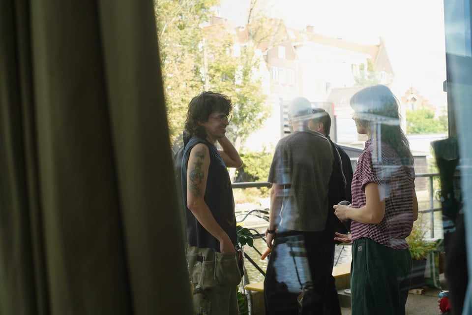 A group of people talking, framed through the pane of a glass window. Behind them - an Amsterdam canal view.