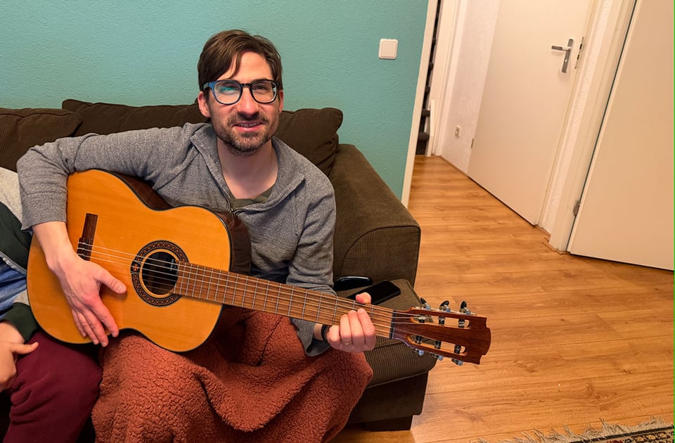 A man sitting on a couch holds a new to him guitar.