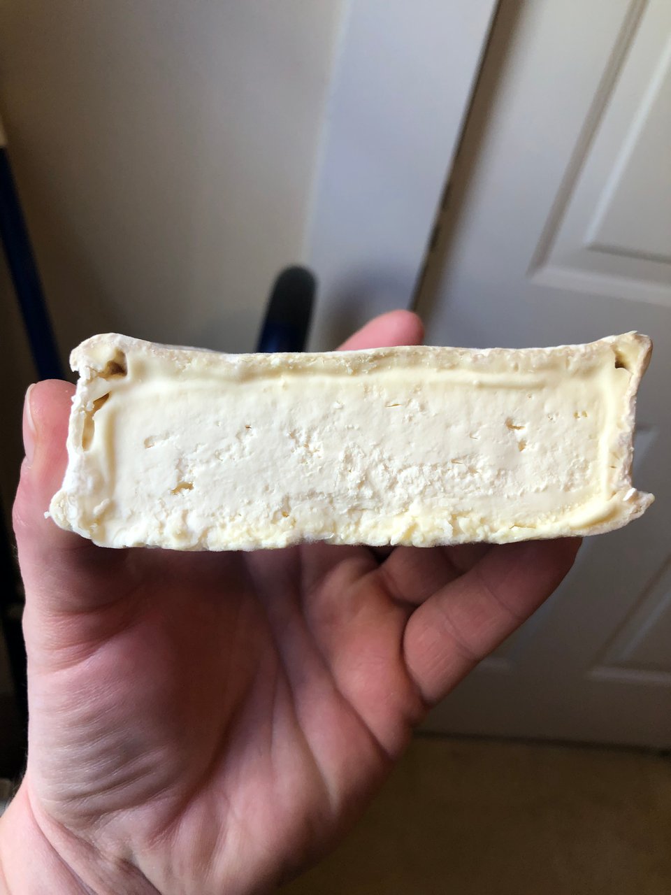 a half-cheese being held aloft by a pink hand, showing a clear rind and cream line.