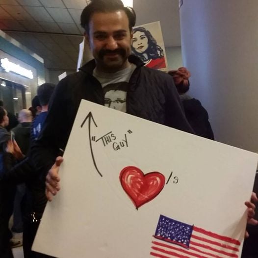 A Muslim man at DFW airport during the Muslim ban protests holding a sign which says "this guy loves America."