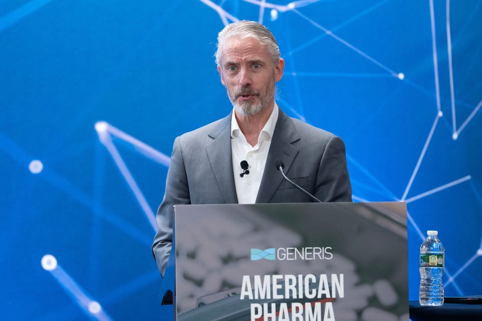 photo of white man in gray suit and white dress shirt, with a lavalliere mic, standing behind a lectern, looking angry