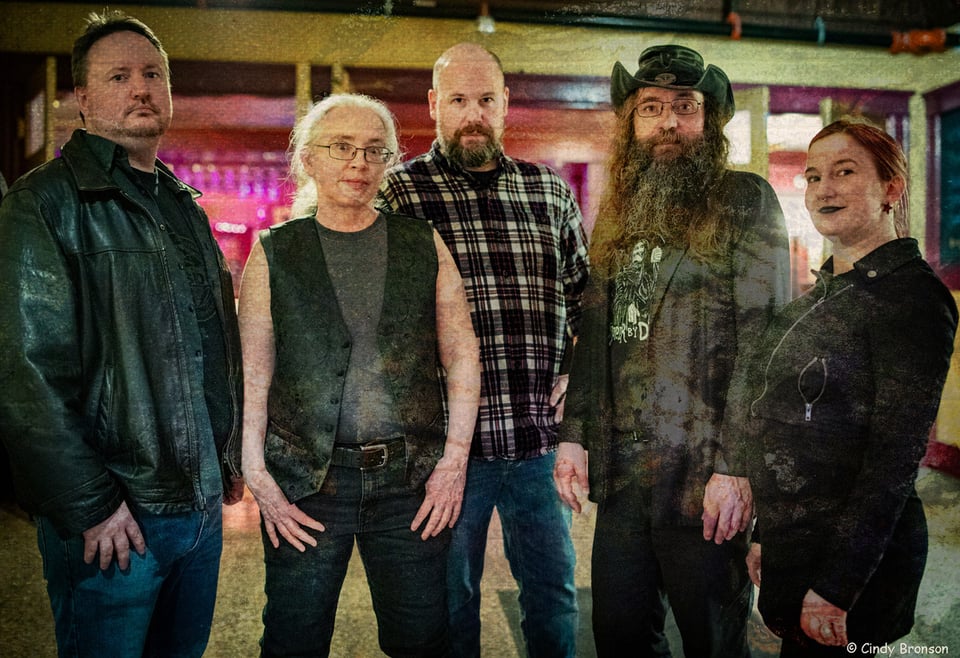 Five people stand together in a line: three men and two women.