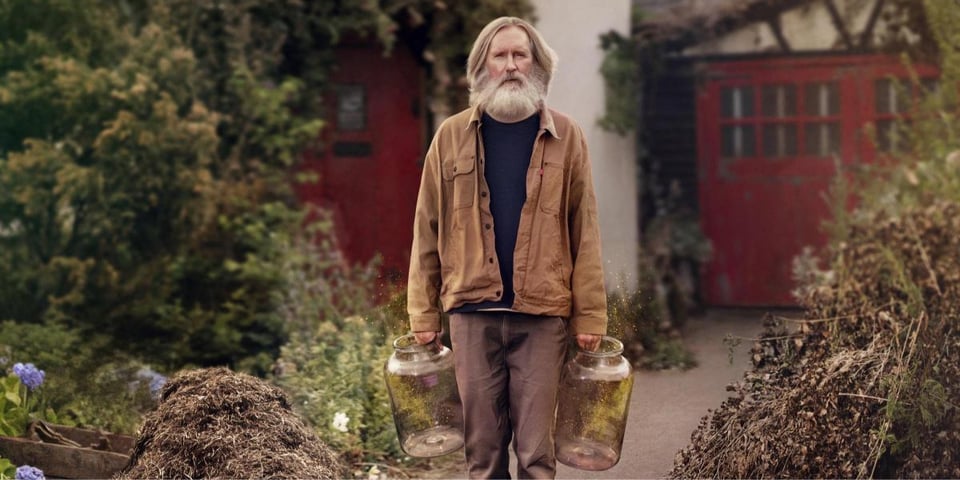 A man in his garden carrying two big jars.