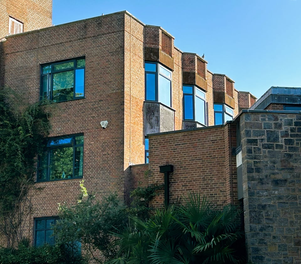 A red brick building with bay windows along one wall. The bricks have been laid in such a way that the mortar forms a faint diamond pattern.