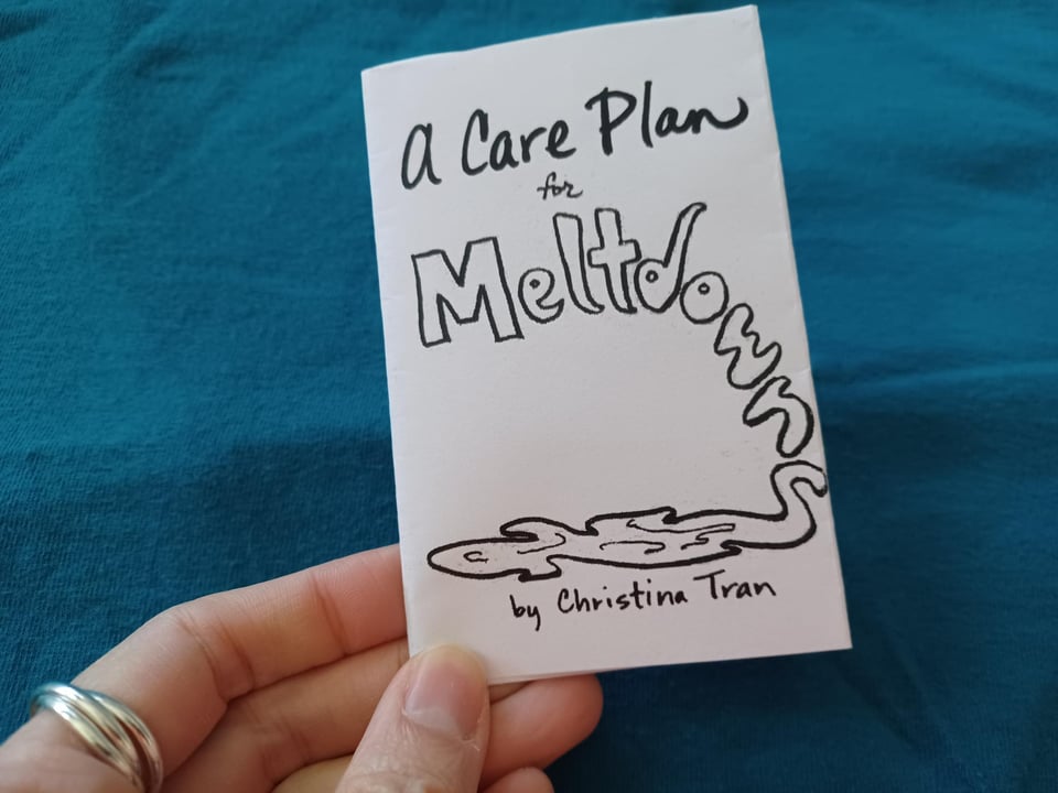 hand with silver ring holds a mini zine with "A Care Plan for Meltdowns" on the cover. Meltdown wordart disintegrates into a puddle.
