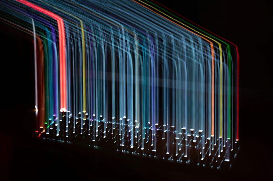 A backlit keyboard moved right and then down in the dark and captured with a long photo exposure. This creates the effect of long lines of different colors of light connecting from the top left of the photo down to the individual keyboard keys that are at he bottom of the image.