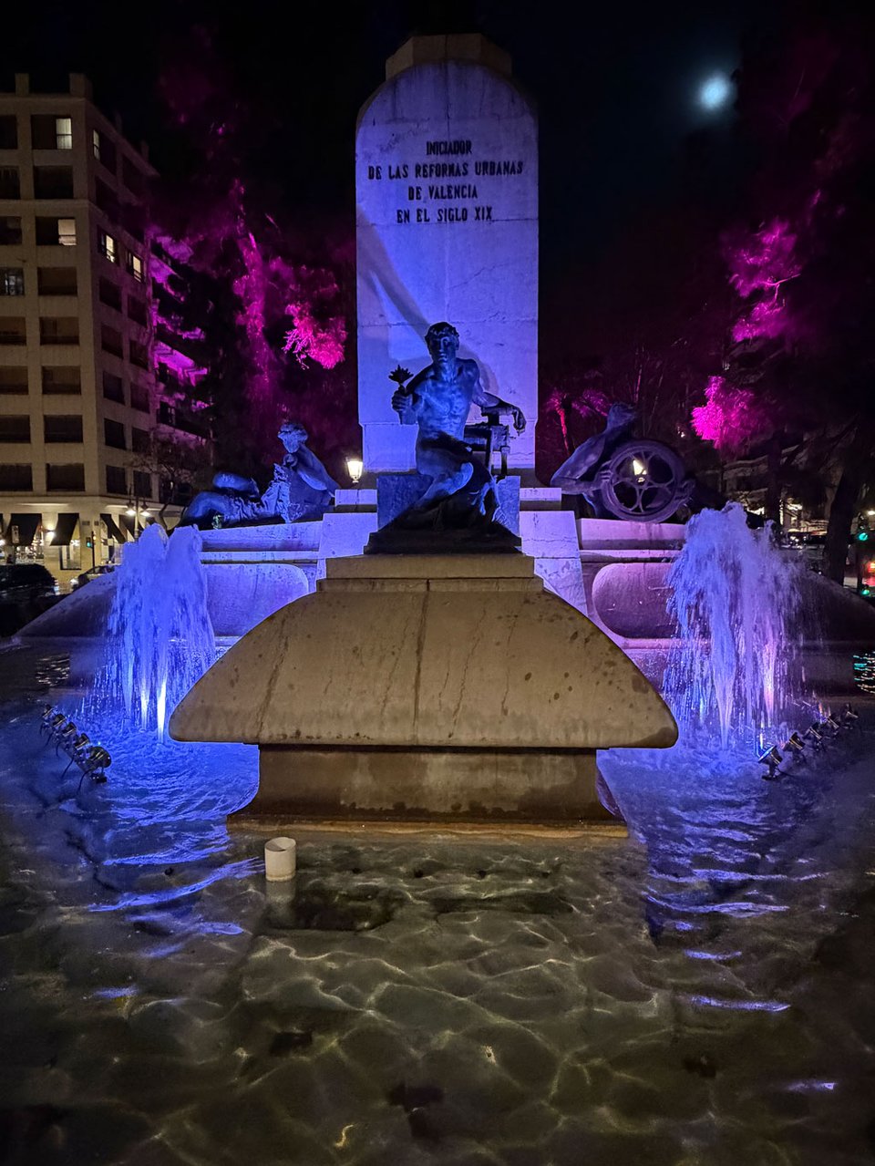 A statue in the middle of a fountain is lit up with purple lights.