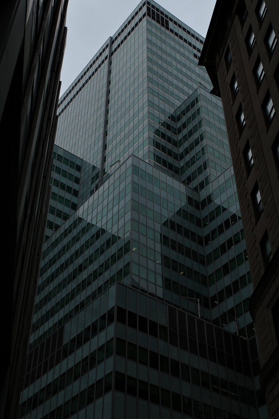 Photograph of a large, multi-sectioned glass skyscraper, shot from 3/4ths view. The shadows and the reflections on the facades make it difficult to ascertain the shape of the building