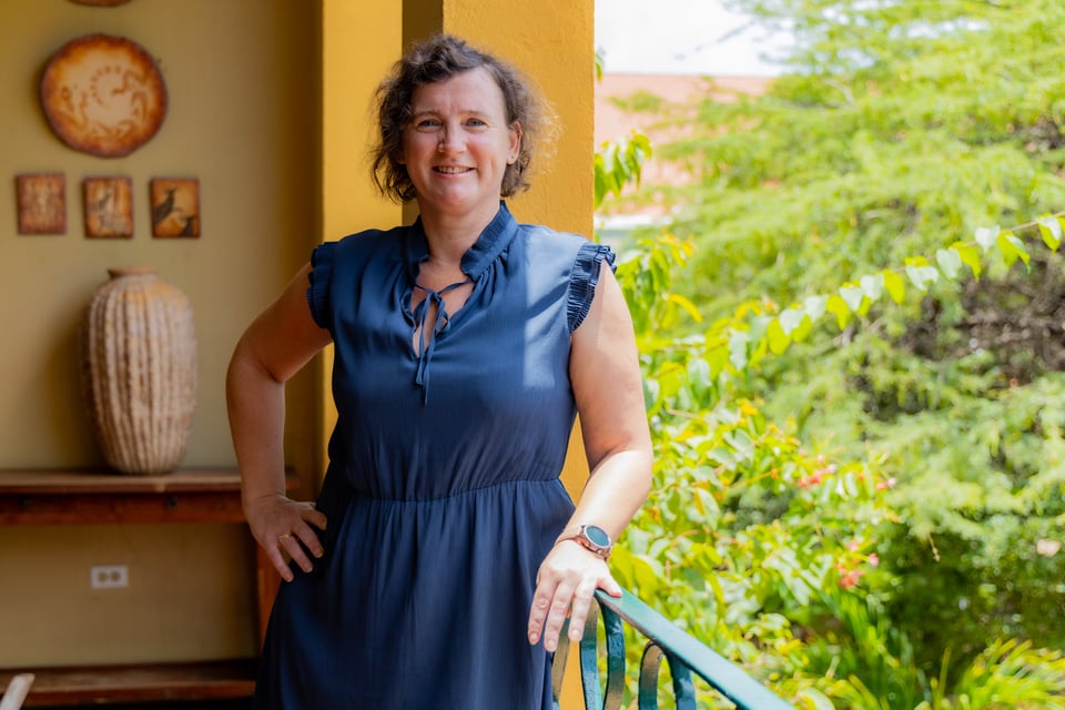 Pauline, a white woman, posing for a campus picture. She is wearing a beautiful blue dress and smiling happily into the camera.