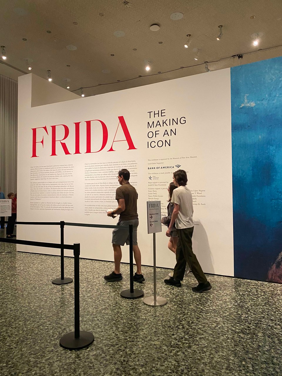 frida: the making of an icon exhibition entrance with three humans walking in front of the signage