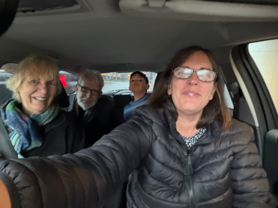 Four people in a car look at the camera before taking off.