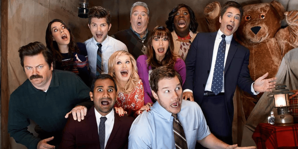 The cast of Parks & Rec pose with a teddy bear.