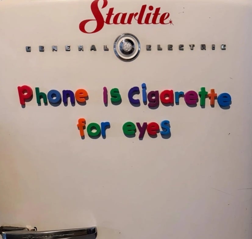 Photo of the front of a retro General Electric Starlite refrigerator. In those multi-coloured fridge magnet letters it reads: Phone is cigarette for eyes