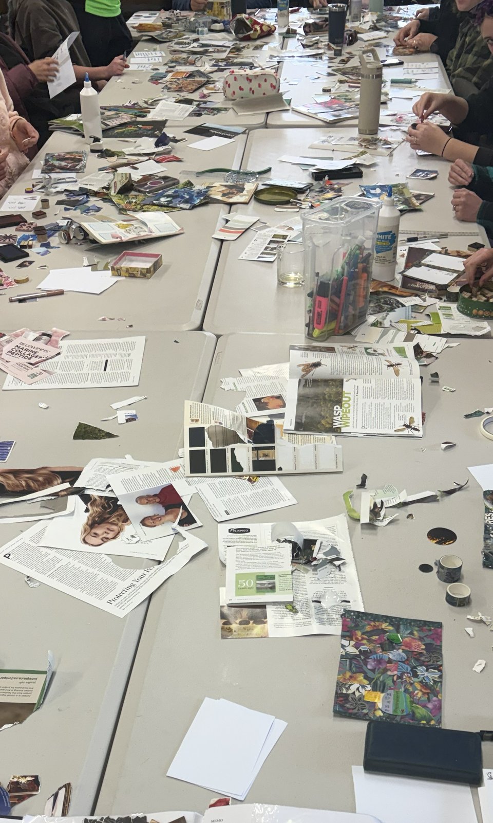 Bird's eye shot of a table of craft - anonymous participant arms and hands working on zines visible.