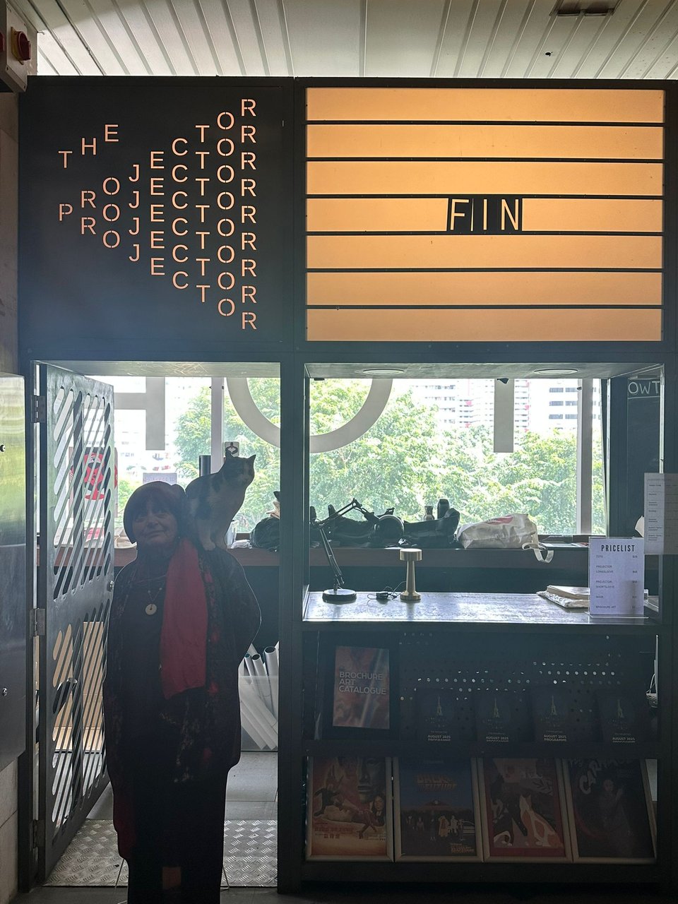 A cardboard standee of a woman with a cat on her shoulder. Behind her is The Projector's box office with the word FIN spelled out in its sign.