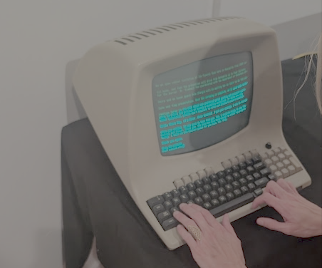 A pair of hands, wearing a cute ring, type at an old-school teletype terminal with clunky keys and a screen with flickering green letters