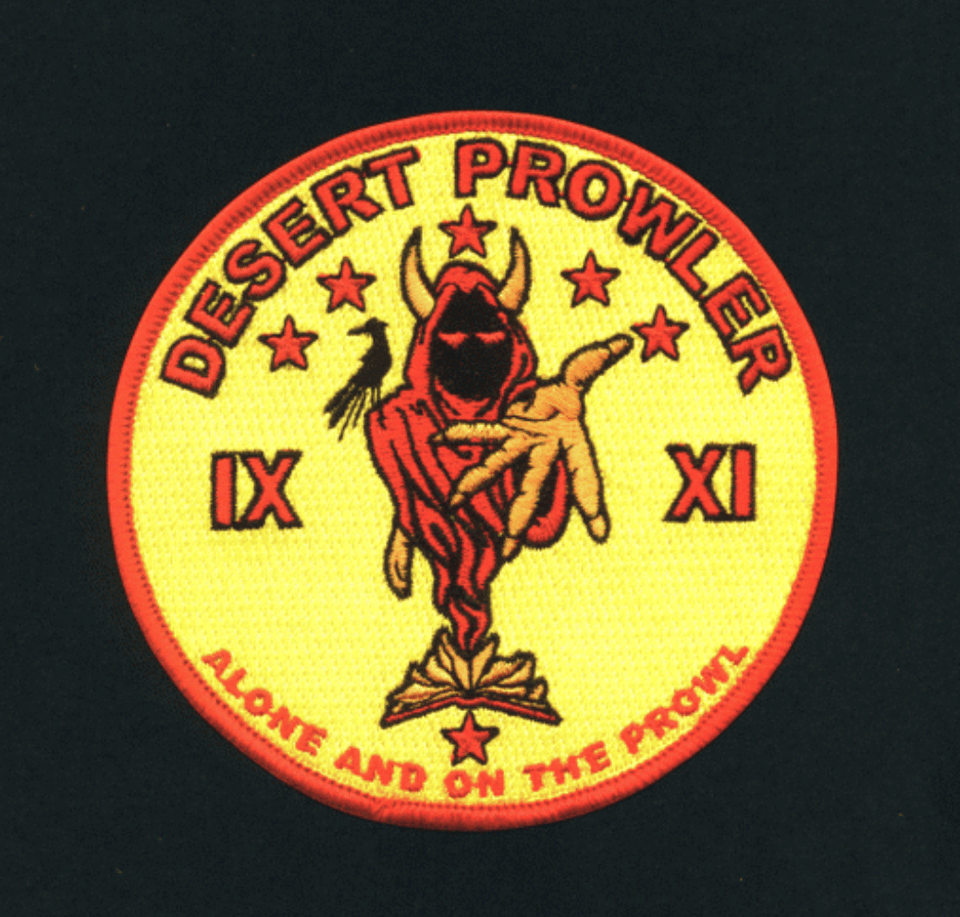 a red and yellow miltary badge featuring a mysterious hooded figure and the words "desert prowler"