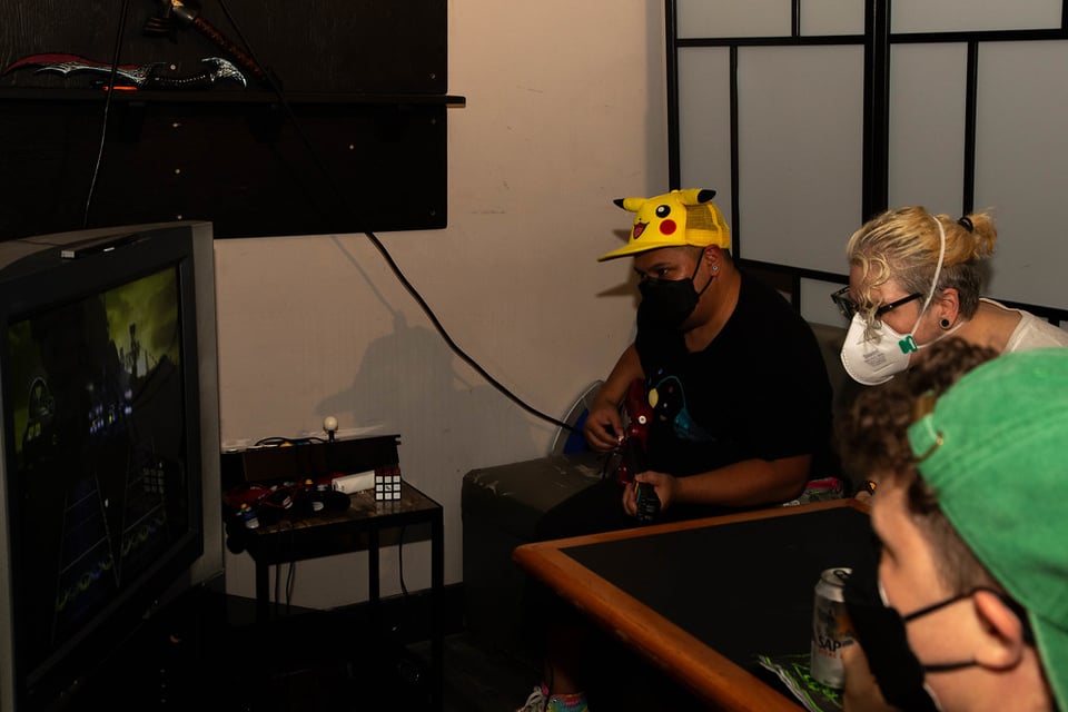 A low-light photo of a person in a green shirt playing video games with other folks. They look serious.