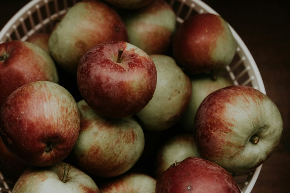 A bucket full of apples with red and green skin and close cut stems.