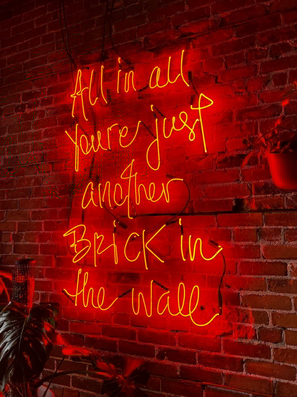 A neon sign that says “all in all you’re just another brick in the wall”