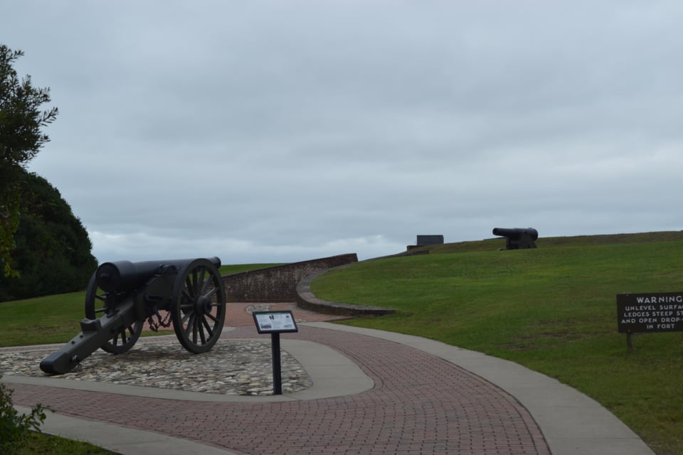 An open patio on which there is a cannon. It is pointed uphill towards a grass rampart, which has a second, smaller cannon on top...pointing down.