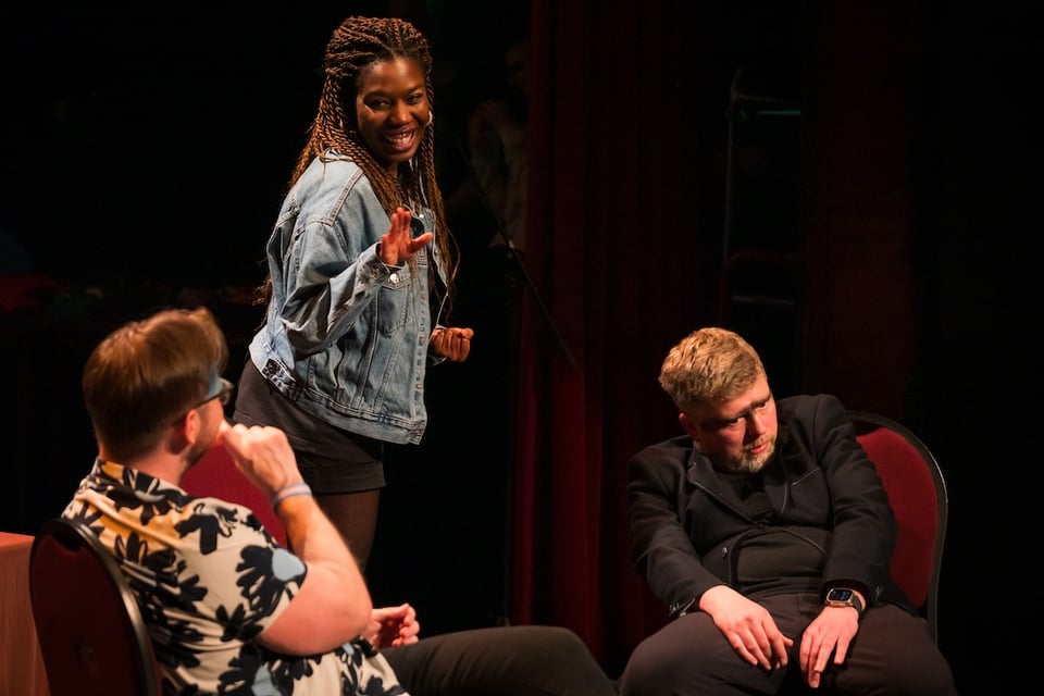 A group of people in a theatre, Chris is slumped down in his chair.