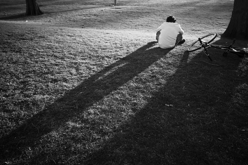 A person sitting next to their bike in the park, looking into the distance.