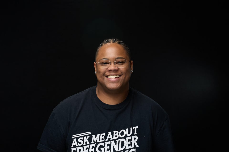 Image of a human smiling with glasses reading Ask Me About Free Gender Affirming Care