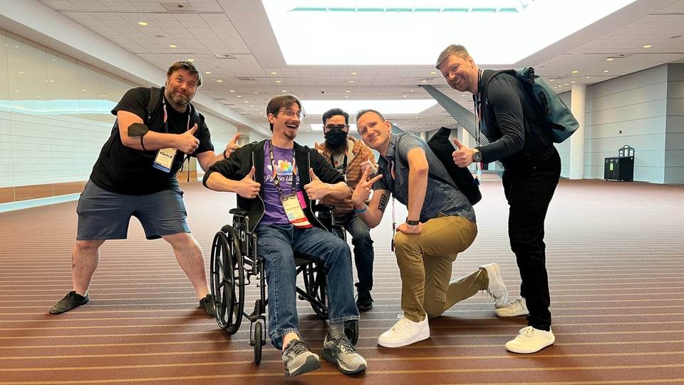 A cheerful KeithTheEE in a wheelchair with cheerful people around him.