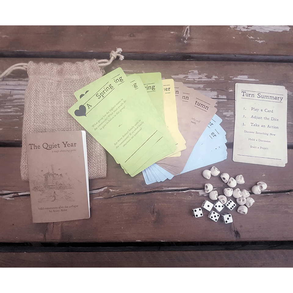 Top-down view of a picnic table with the cotents of the game, including a small burlap sac, several colourful game cards, and small dice.