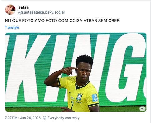 Post de salsa (@santasatelite.bsky.social): NU QUE FOTO AMO FOTO COM COISA ATRAS SEM QRER (fotografia de vini junior todo suado, jogador negro retinto de cabelo crespo curto, blusa do brasil amarela numero 7, apontando pra cabeça comemorando gol acho, atrás dele está cortado um letreiro com destaque em “king” - traduzindo, rei.)