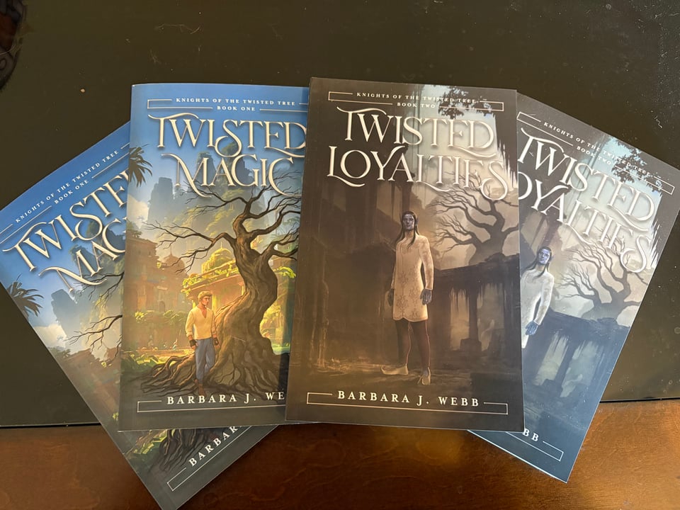 A fan of books showing the covers of Twisted Magic and Twisted Loyalties